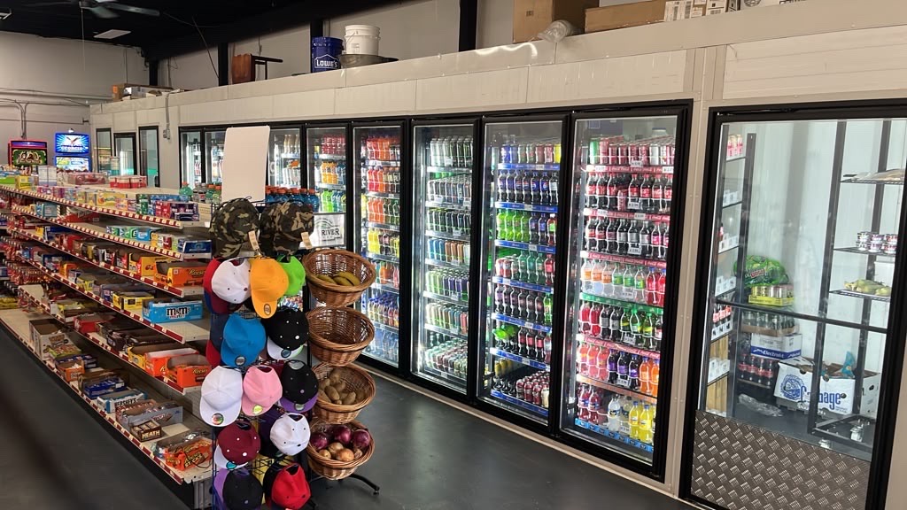 A long run of glass-door coolers stocked with bottled and canned drinks beside the snack aisle.