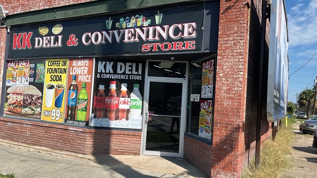 The KK Deli storefront with its illuminated awning sign above the window displays.